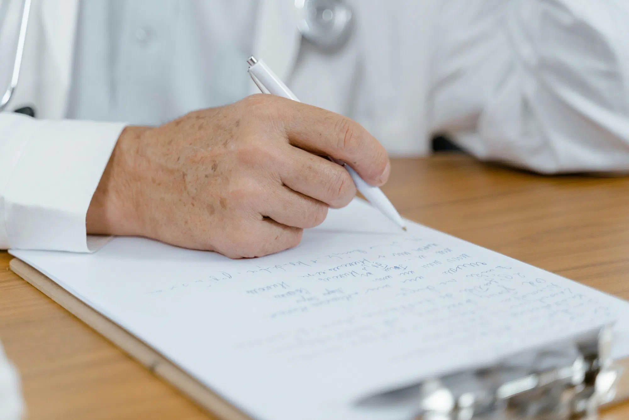 Eine Hand schreibt mit einem Stift auf ein Klemmbrett